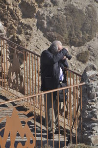 Rear view of man photographing on railing