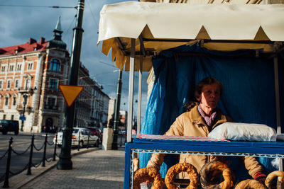 Man sitting on seat in city against buildings