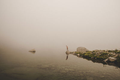 Distant view of man standing by sea during foggy weather