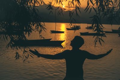 Silhouette man standing against lake during sunset