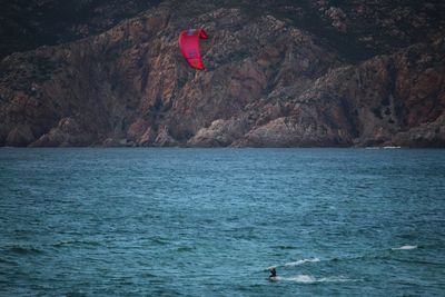 Person kiteboarding in sea against mountains