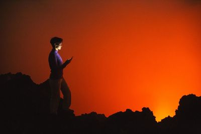 Woman using smartphone against orange sky