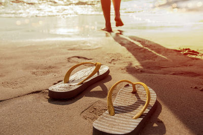Flip-flops on shore with woman in background at beach