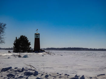 Lighthouse by sea against clear blue sky