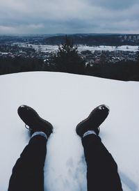 Low section of man sitting on snow covered mountain against cloudy sky