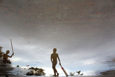 Reflection of boy holding cricket bat in puddle