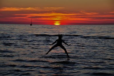 Silhouette person in sea against sky during sunset