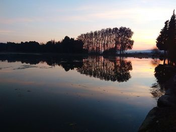 Silhouette trees by lake against sky during sunset