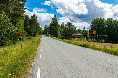 Road sign by trees against sky