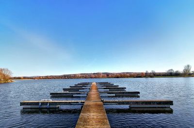 Pier over lake against clear blue sky