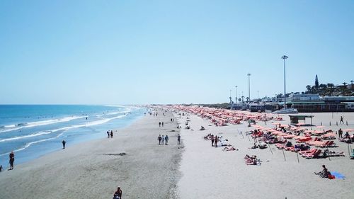 People at beach against clear blue sky