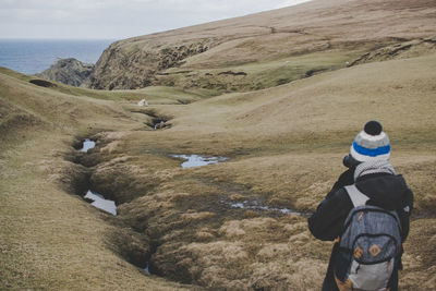 Rear view of man climbing on landscape against sky