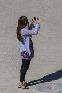 Full length of woman photographing through smart phone during sunny day