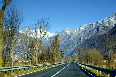 Road amidst snowcapped mountains against clear sky
