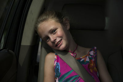 Young smiling blonde girl sits in back seat of car, window light