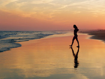 Silhouette woman standing at beach against sky during sunset