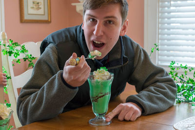 Portrait of young man having ice cream while sitting at table in cafe