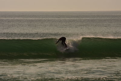 Man surfing in sea against sky during sunset