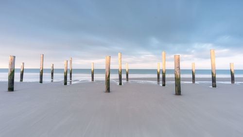 Wooden posts on sea against sky