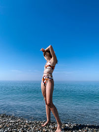Full length of woman standing at beach against blue sky