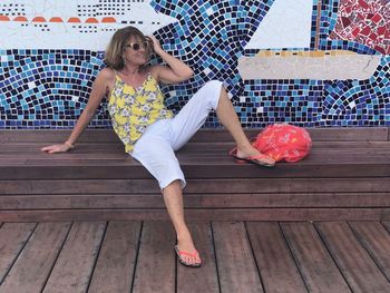 Full length of smiling senior woman sitting against tiled wall