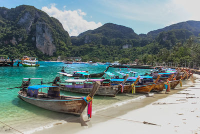 Boats moored on sea by mountains against sky