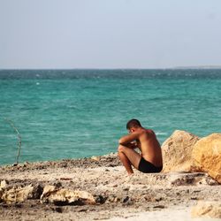 Side view of young woman standing at beach against clear sky