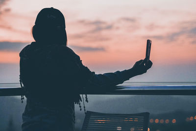 Woman taking selfie against sky during sunset