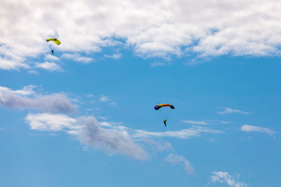 Low angle view of people paragliding against sky