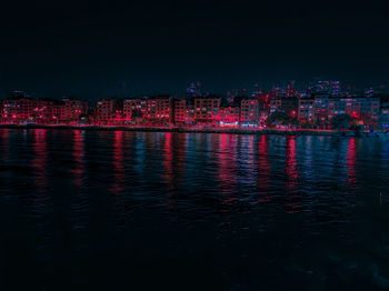 Illuminated city by river against sky at night