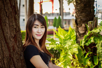 Portrait of smiling young woman against tree trunk