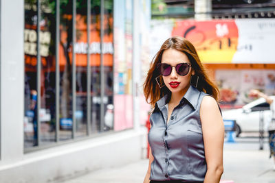 Portrait of beautiful young woman wearing sunglasses on footpath in city