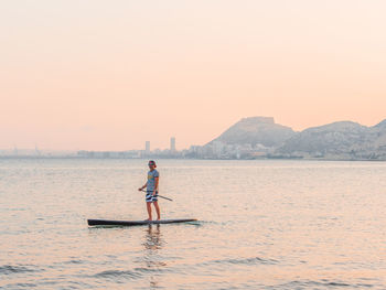 Sporty man swimming on surfboard paddle looking away in alicante spain