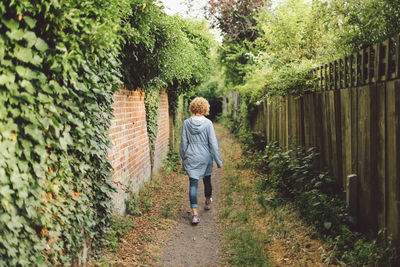 Full length rear view of woman walking on pathway amidst wall