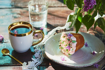 Summer outdoor branch with a cup of coffee, beautiful cupcake, glass of water and bright flowers. 