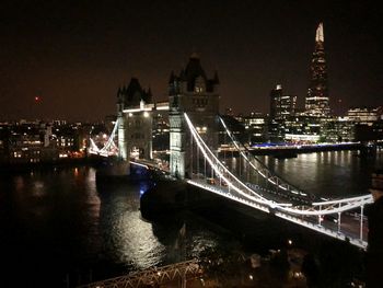 Illuminated bridge over river by buildings in city at night