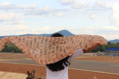Rear view of woman flying scarf against sky