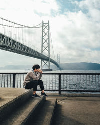 Man sitting on bridge against sky