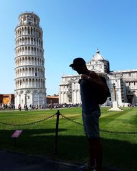 Rear view of man standing by statue in city against clear sky