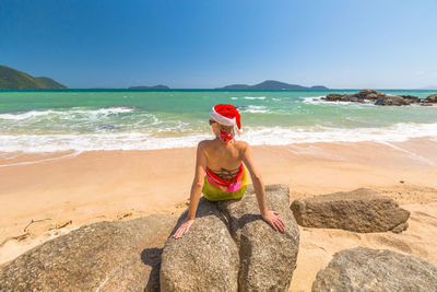 Woman sitting on rock at beach against sky