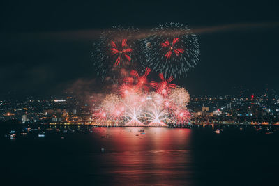 Firework display over illuminated city against sky at night