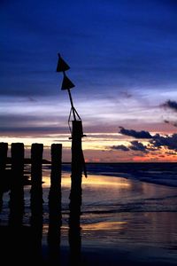 Silhouette wooden posts on beach against sky at sunset