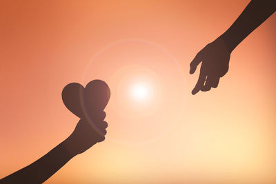 Cropped image of silhouette hands with heart shape against orange sky