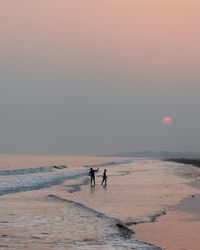 People on beach against sky during sunset