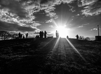 Back lit people on grassy field in park against sky