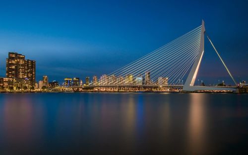 Illuminated city by sea against sky at night