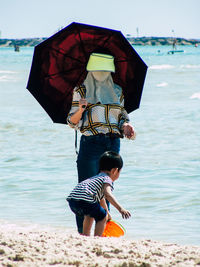Rear view of woman holding umbrella on beach