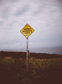 Road sign on field against sky