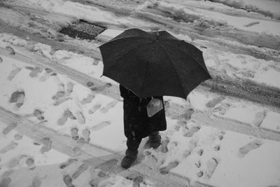 Rear view of man standing on snow covered landscape during rainy season