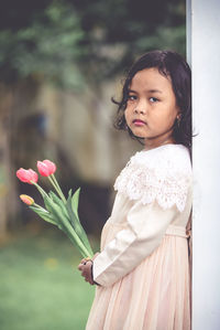 Portrait of woman with pink flower standing against blurred background